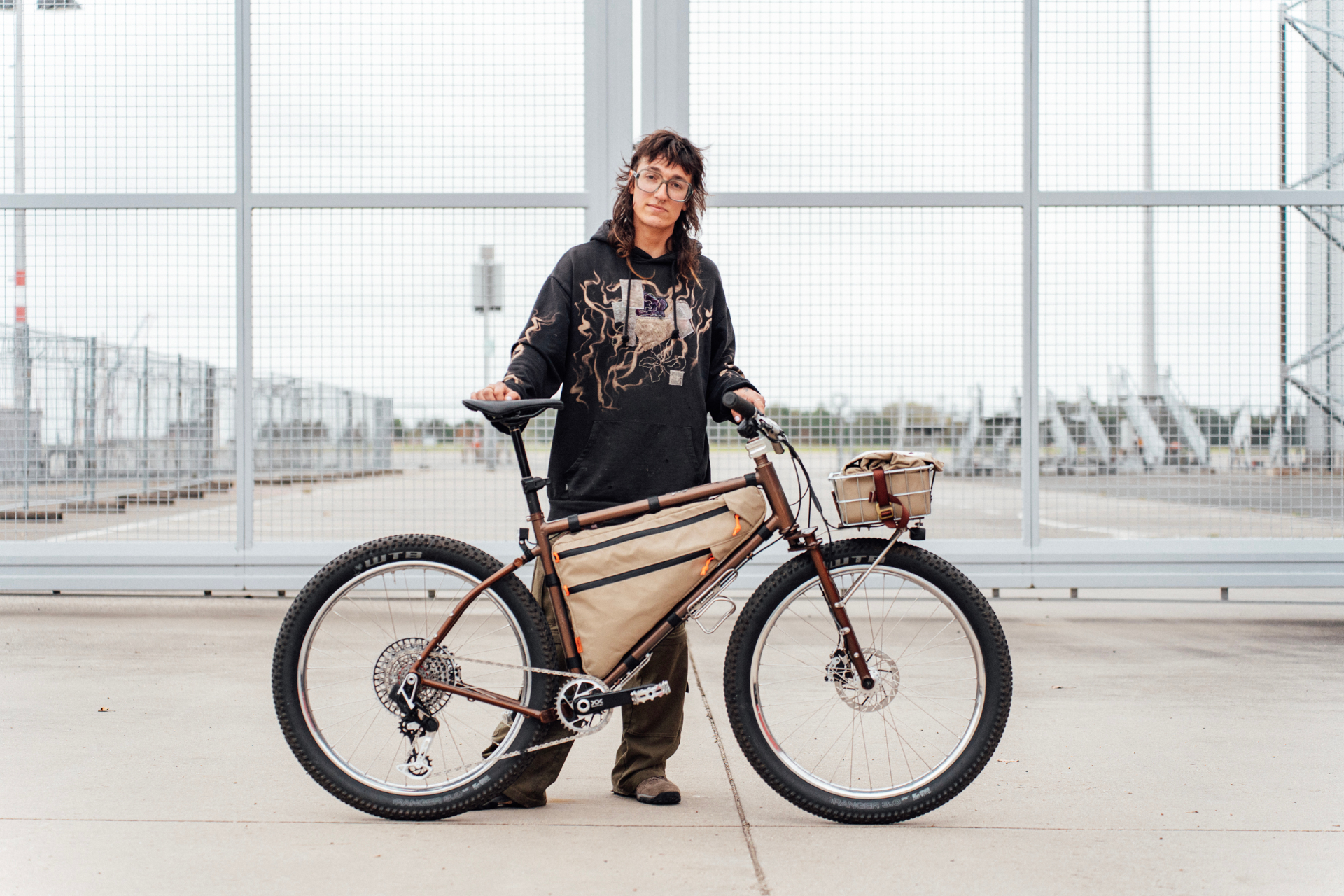 Framebuilder standing with their custom brown steel bike outside Dresden International Airport, with their full head visible in frame