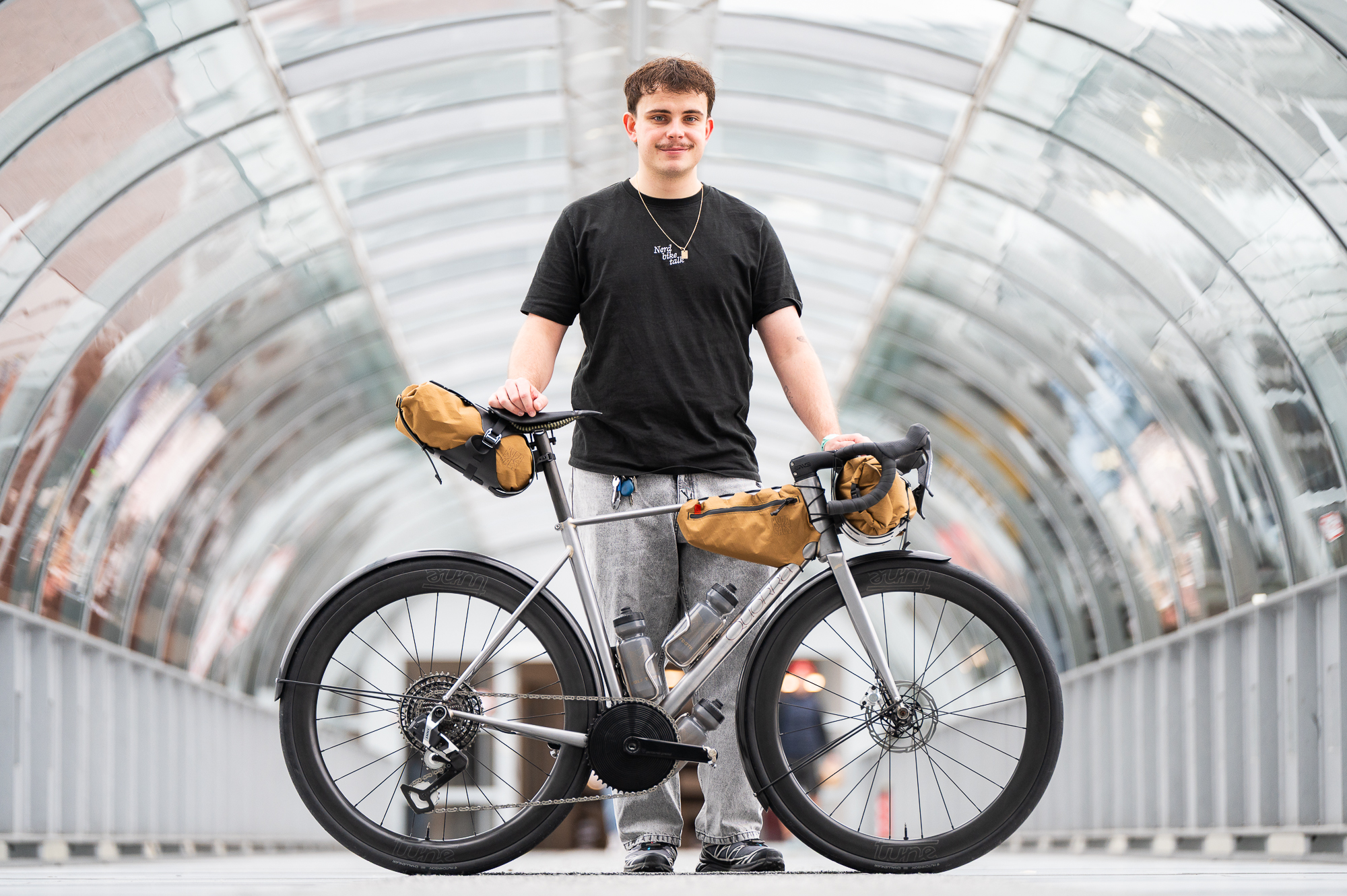 A maker standing behind a titanium bikepacking bicycle in a glass tunnel