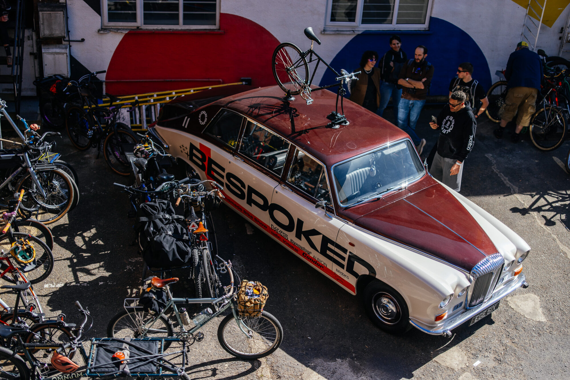 A vintage Daimler in BESPOKED livery parked outside the venue with bikes on the roof