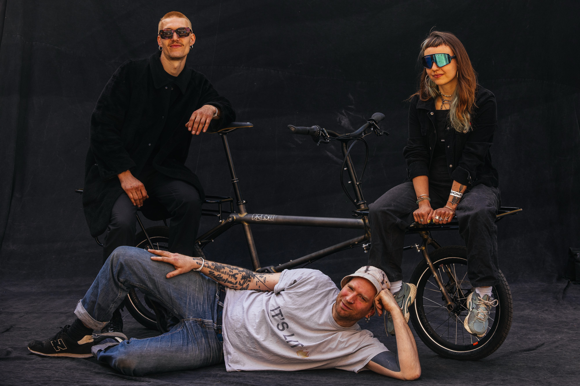 Three makers posing with a Drust Broom cargo bike against a black backdrop
