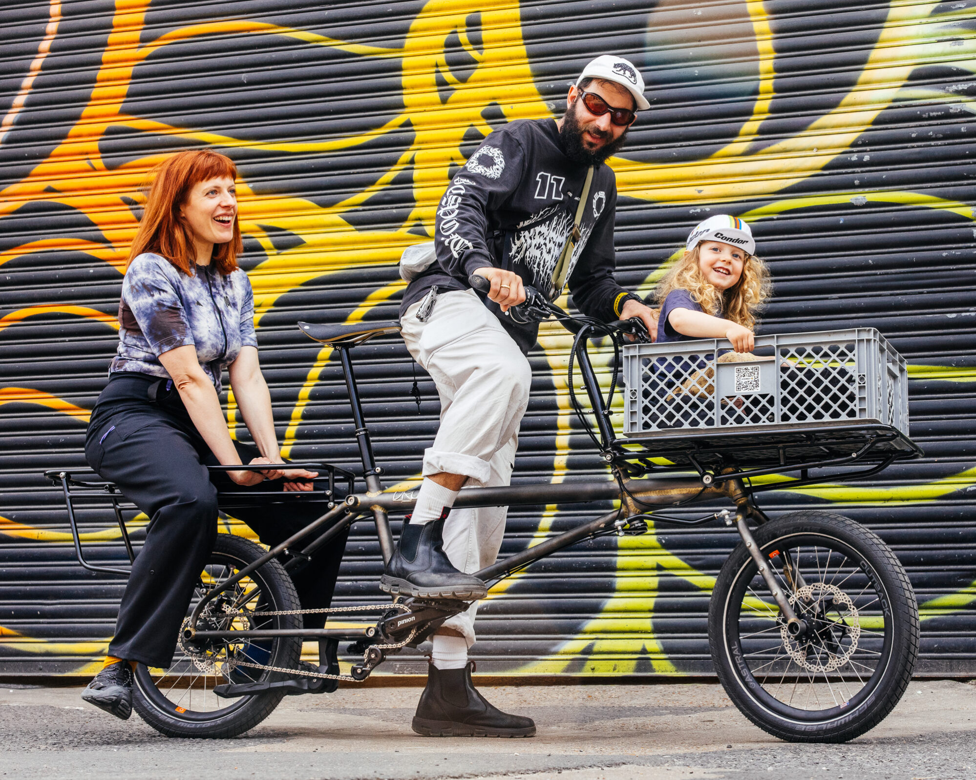 Riders and their family on a custom cargo bike in front of a graffiti shutter